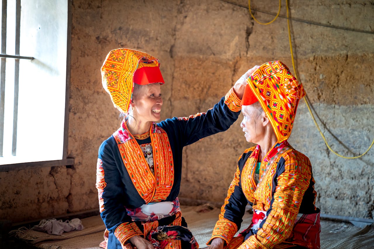 Two women in vibrant traditional clothing share a moment indoors, showcasing cultural heritage.